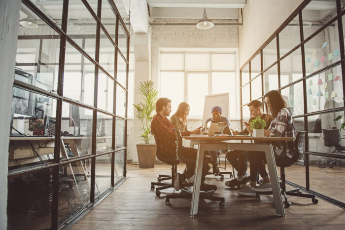 Full length concentrated female and men partners looking at mobile and working with notebook computers while locating at desk. Orderly team concept