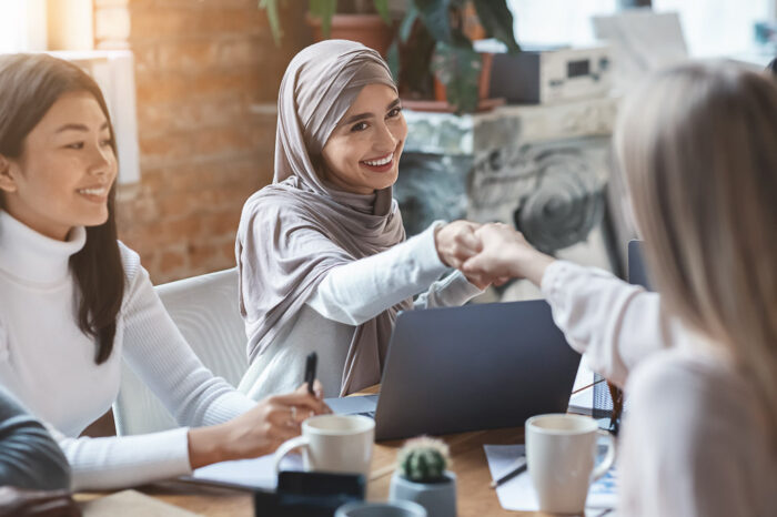 Two multiracial girls business colleagues shaking hands during group meeting in office, close up